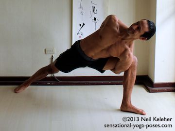 bound side angle pose, front view. In this standing bound pose, right knee is bend 90 degrees with thigh horizontal. Left knee is straight. Right arm is reaching behind the back. Left hand is reaching beneath the thigh and then up behind the back to grab the right hand. Feet are flat on the floor with left foot turned out 90 degrees. Model Neil Keleher, Sensational Yoga Poses.