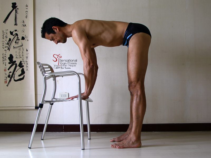 Standing hamstring stretch with hands on a chair and arms engaged to support the weight of upper body. Hamstrings are relaxed with knees straight. Neil Keleher, Sensational Yoga Poses.
