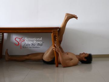 Supine hamstring stretch using a table as a prop. Neil Keleher. Sensational Yoga Poses.