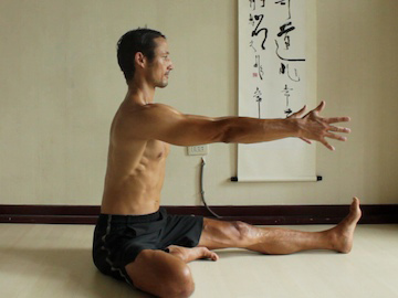 janu sirsasana prep position, sitting upright with arms reaching forwards.