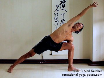 ashtanga yoga poses, utthitta parsvokonasana, side angle yoga pose left side. In left side angle yoga pose the left knee is bent 90 degrees. The right knee is straight. Both feet are flat on the floot and the left foot is turned out 90 degrees. The right foot is slightly turned in. The right arm reaches over the head and the left hand rests on the floor outside the left foot. Both elbows are straight. The knee can push back against the arm. Model Neil Keleher, Sensational Yoga Poses.