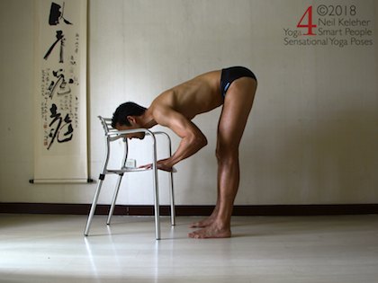Standing forward bend with knees straight and hands on a chair. Hamstrings are kept relaxed so that they can be stretcheds as the elbows are bent and the forward bend increase. Neil Keleher, Sensational Yoga Poses.
