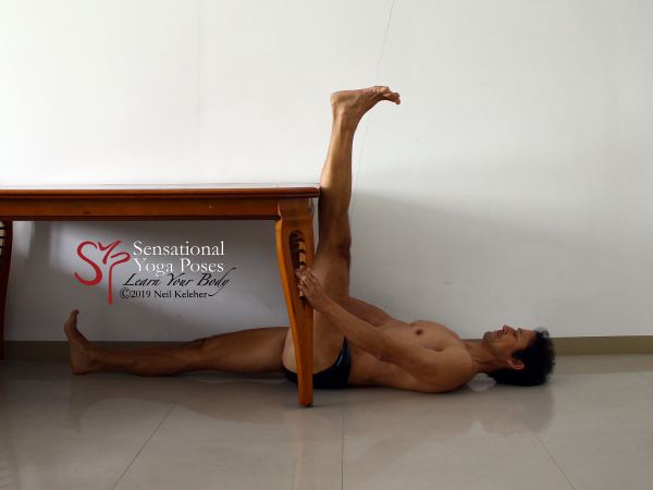 Supine hamstring stretch underneath a table. Rest a leg against the edge of the table to stretch it. Neil Keleher. Sensational Yoga Poses.